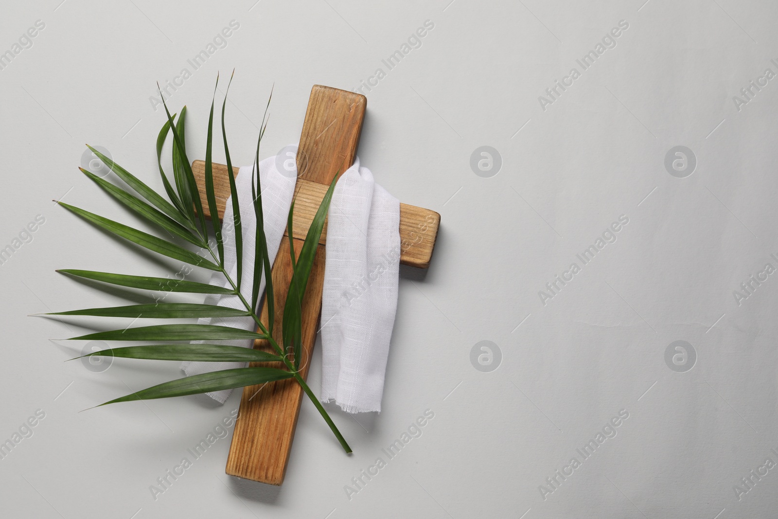 Photo of Wooden cross, white cloth and palm leaf on light grey background, top view with space for text. Easter attributes