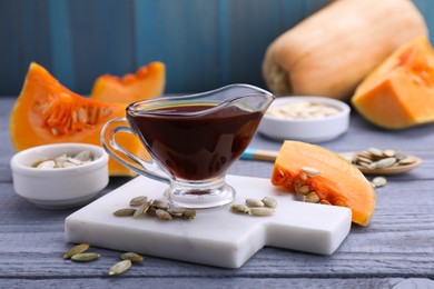 Photo of Fresh pumpkin seed oil in glass sauceboat on grey wooden table