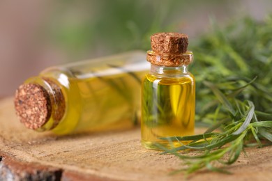 Bottles of essential oil and fresh tarragon leaves on wooden stump, closeup