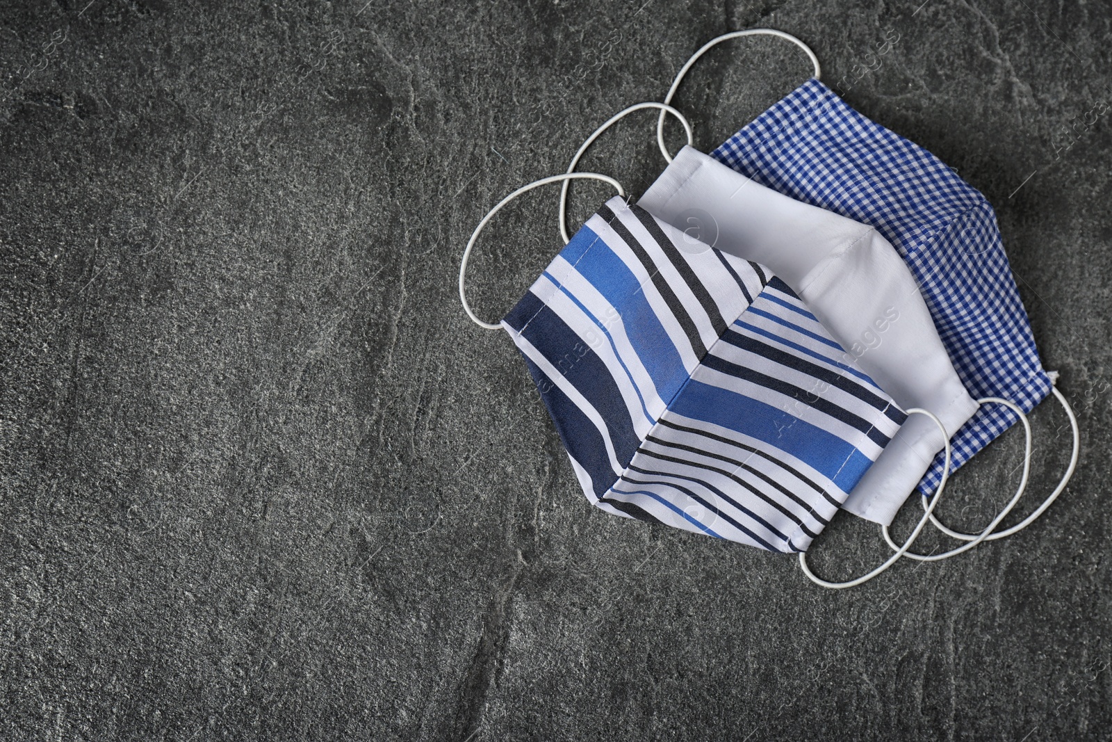 Photo of Homemade protective face masks on grey stone table, flat lay. Space for text