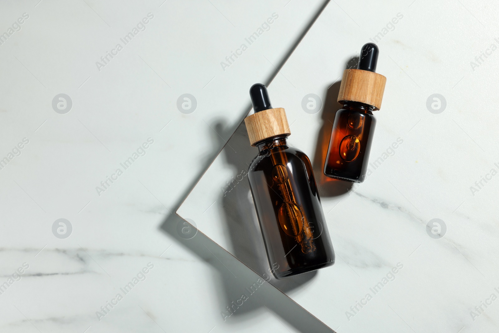 Photo of Glass bottles of essential oil on white marble table, flat lay