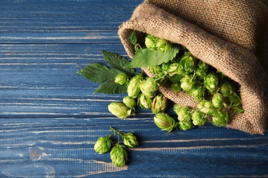 Photo of Sackcloth bag with fresh green hops on wooden background, top view with space for text. Beer production