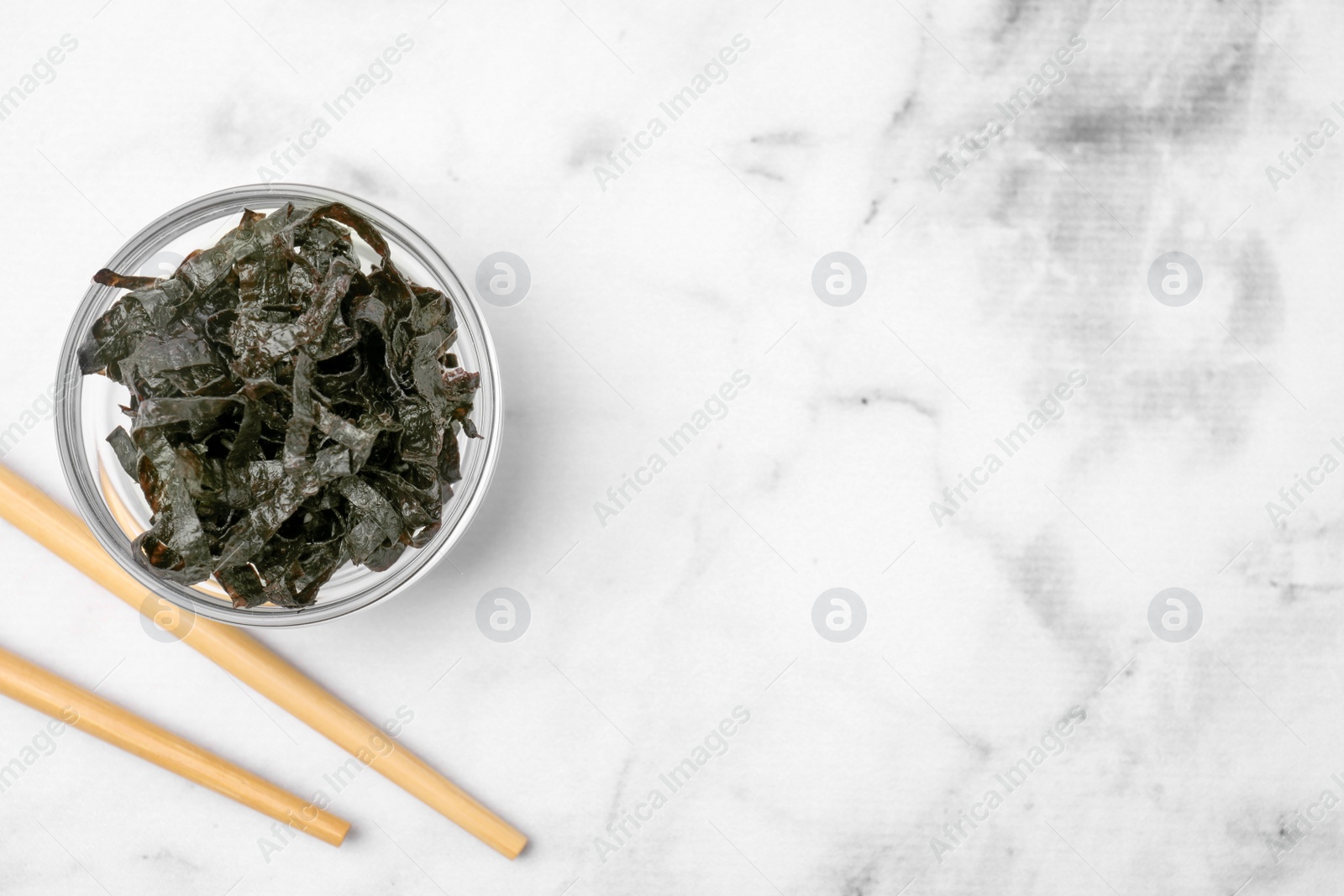 Photo of Chopped nori sheets with chopsticks on white marble table, flat lay. Space for text