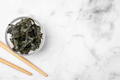 Photo of Chopped nori sheets with chopsticks on white marble table, flat lay. Space for text