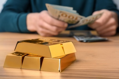 Photo of Stacked gold bars and man counting money at table, closeup. Space for text