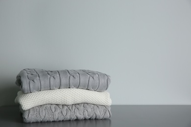 Photo of Stack of folded knitted sweaters on grey table. Space for text