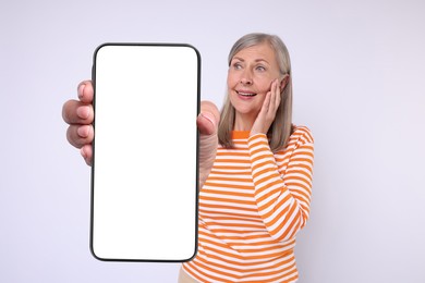 Happy mature woman showing mobile phone with blank screen on white background. Mockup for design