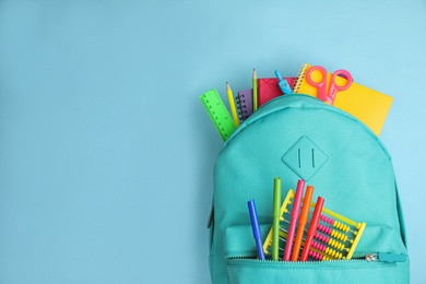 Stylish backpack with different school stationary on light blue background, top view. Space for text