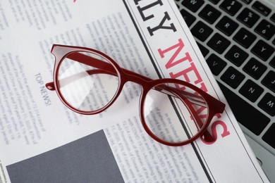 Newspaper and glasses on laptop, top view