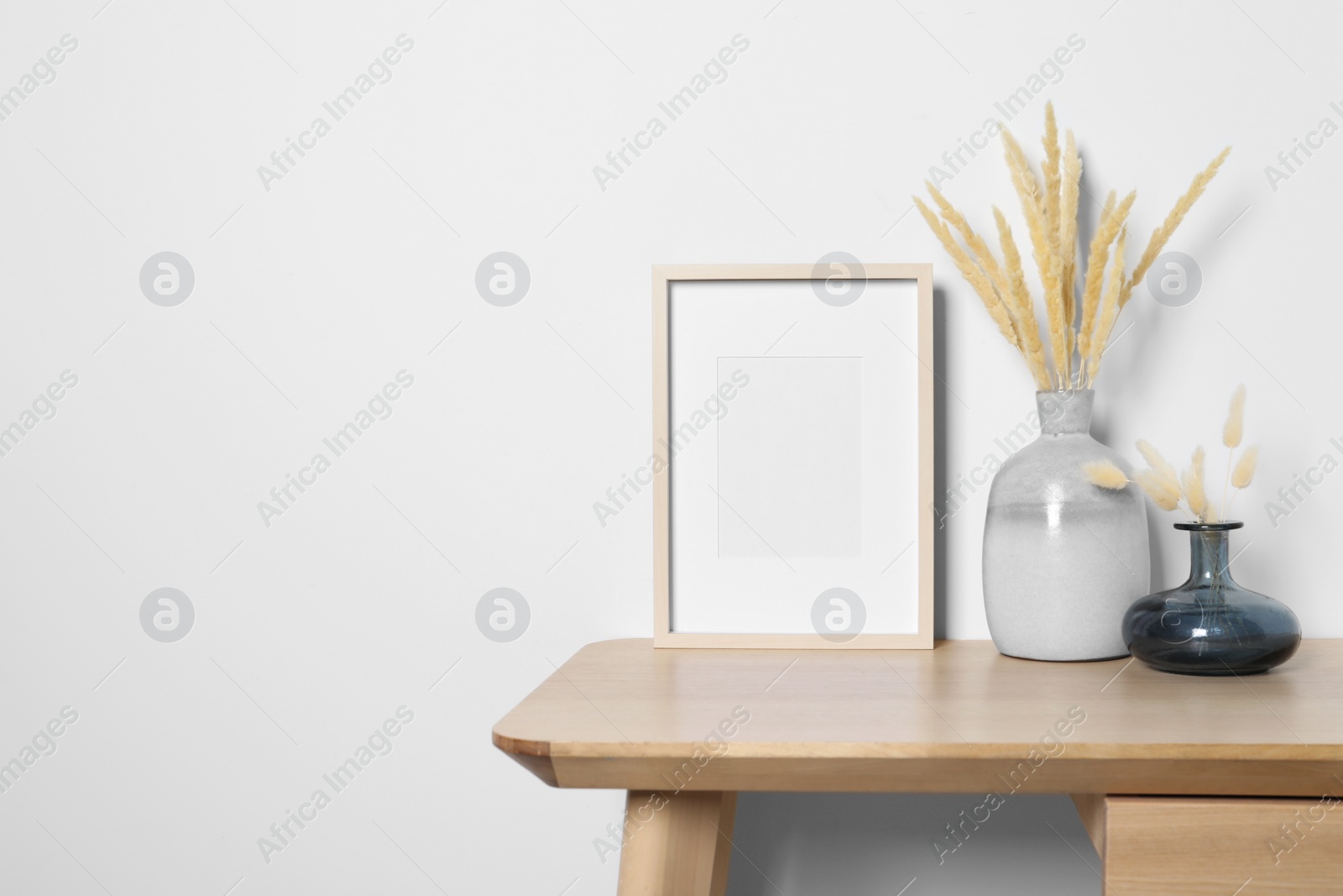 Photo of Empty photo frame and vases with dry decorative spikes on wooden table. Mockup for design