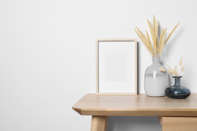 Empty photo frame and vases with dry decorative spikes on wooden table. Mockup for design