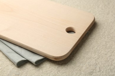 Wooden cutting board and napkin on beige table, closeup