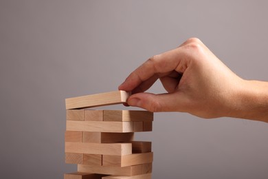 Photo of Playing Jenga. Man building tower with wooden blocks on grey background, closeup