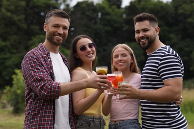 Photo of Happy friends clinking glasses with cocktails outdoors