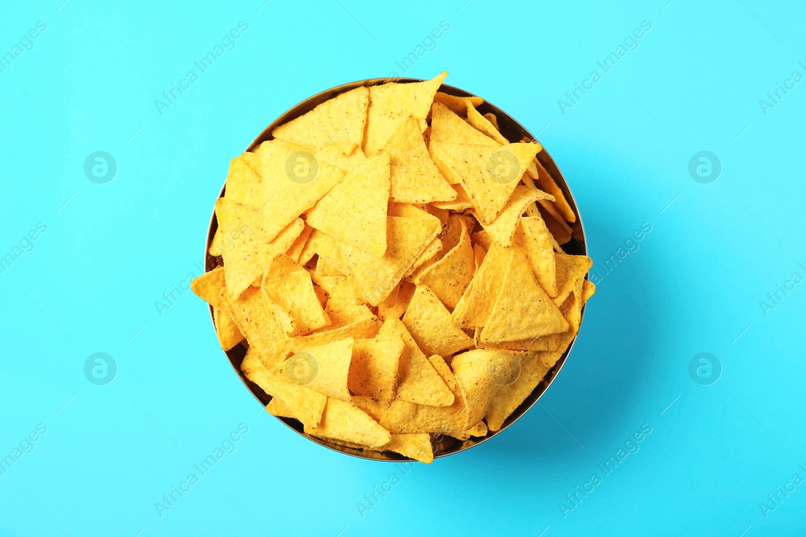 Photo of Tasty mexican nachos chips in metal bowl on blue background, top view