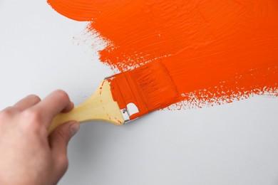Photo of Man applying orange paint with brush on white background, closeup