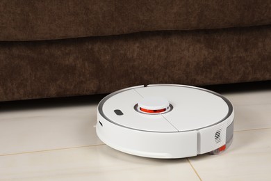 Photo of Robotic vacuum cleaner on white tiled floor near sofa indoors