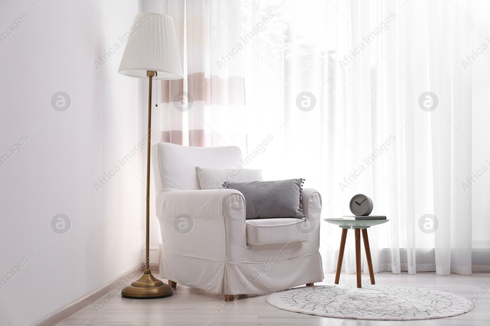 Photo of Comfortable armchair and lamp near window with elegant curtains in room