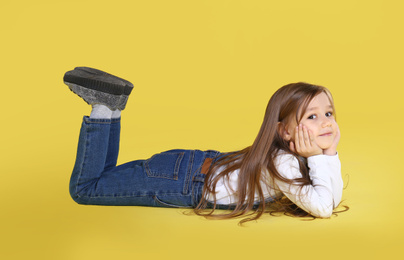Photo of Cute little girl lying on yellow background