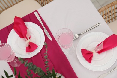 Table setting. Glasses of tasty beverage, plates with pink napkins and cutlery in dining room, above view