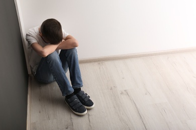 Photo of Upset boy sitting on floor indoors. Space for text