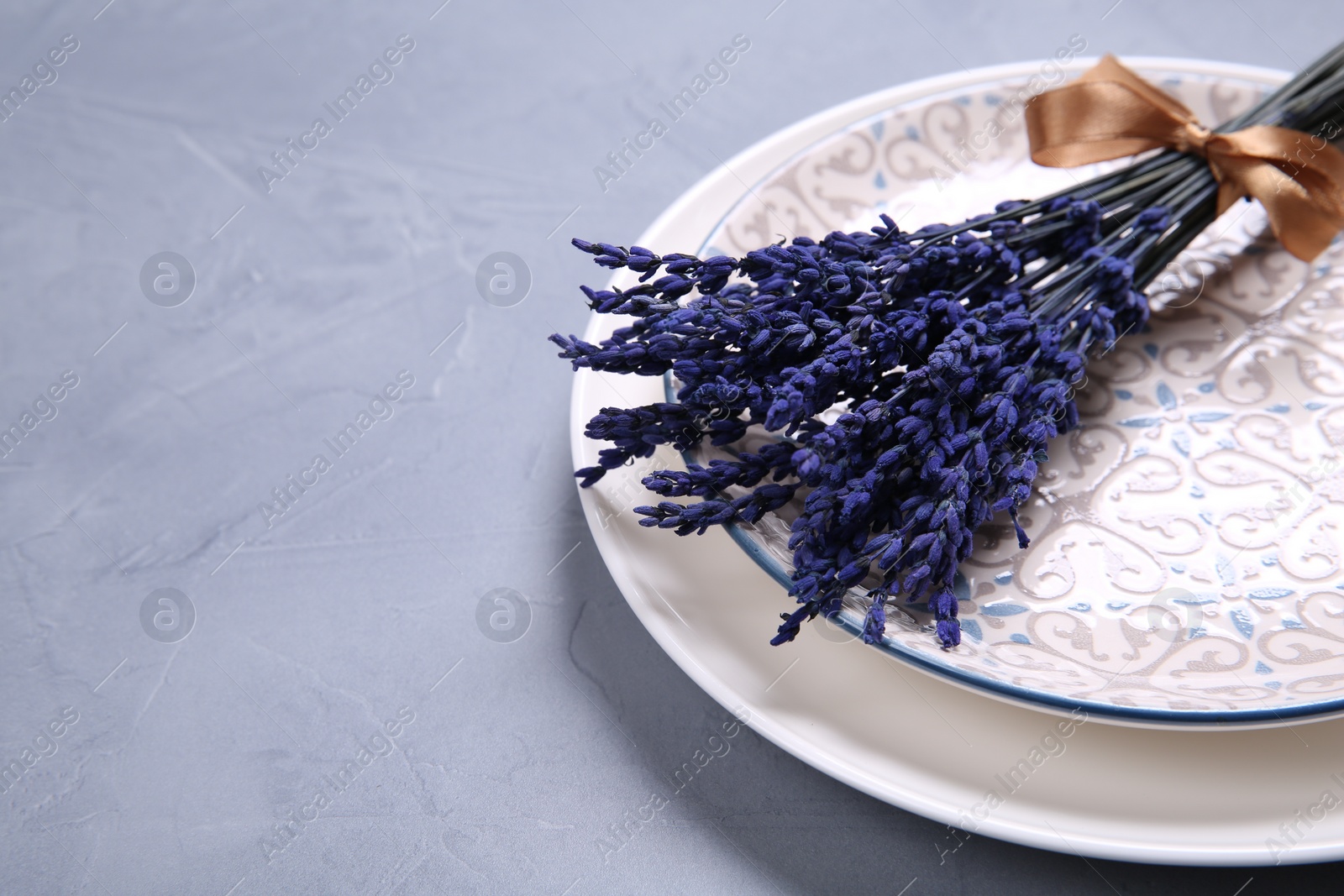 Photo of Bouquet of beautiful preserved lavender flowers and plates on light grey textured table, closeup. Space for text