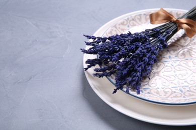 Photo of Bouquet of beautiful preserved lavender flowers and plates on light grey textured table, closeup. Space for text