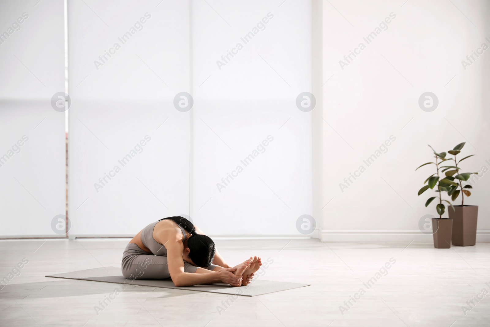 Photo of Young woman practicing seated forward bend asana in yoga studio. Paschimottanasana pose