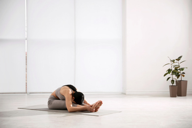 Photo of Young woman practicing seated forward bend asana in yoga studio. Paschimottanasana pose
