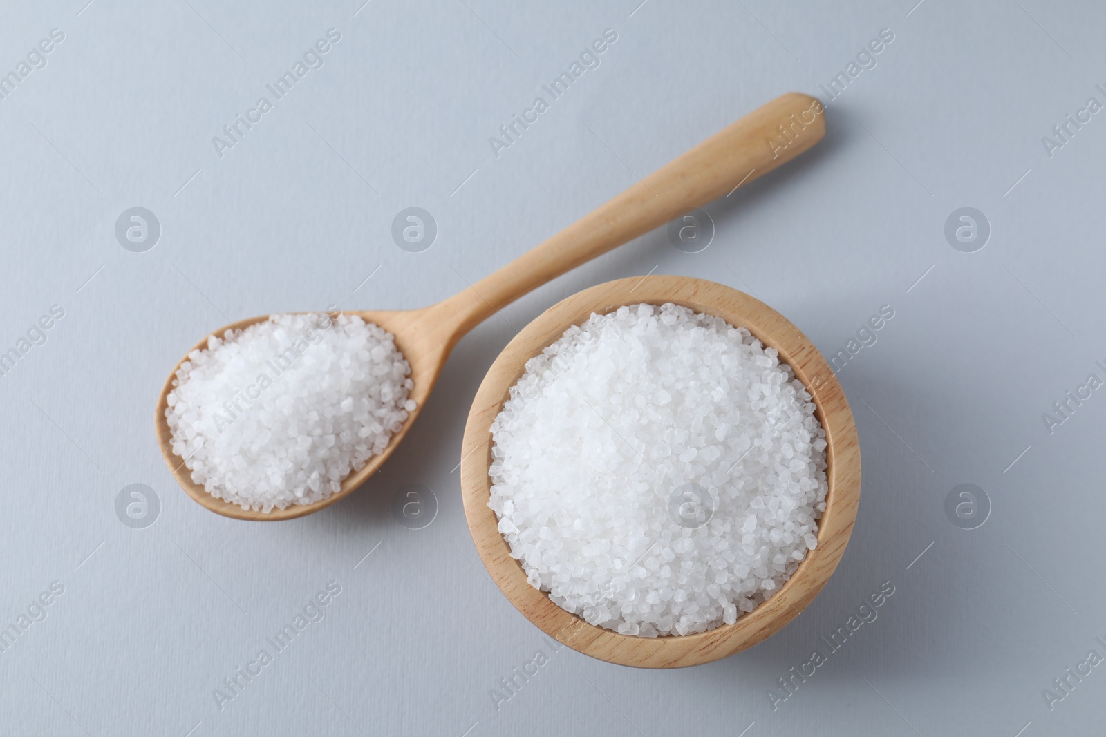 Photo of Organic white salt in bowl and spoon on light grey background, top view