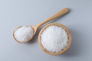 Photo of Organic white salt in bowl and spoon on light grey background, top view