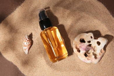 Bottle of serum, seashell and stone on sand against brown background, flat lay