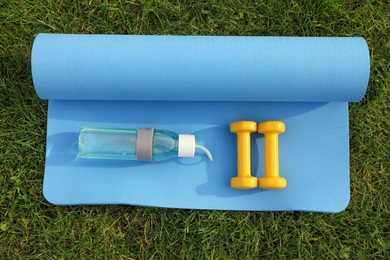 Photo of Dumbbells, bottle of water and fitness mat on green grass, flat lay. Morning exercise