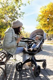 Photo of Happy mother with her baby son in stroller outdoors on autumn day