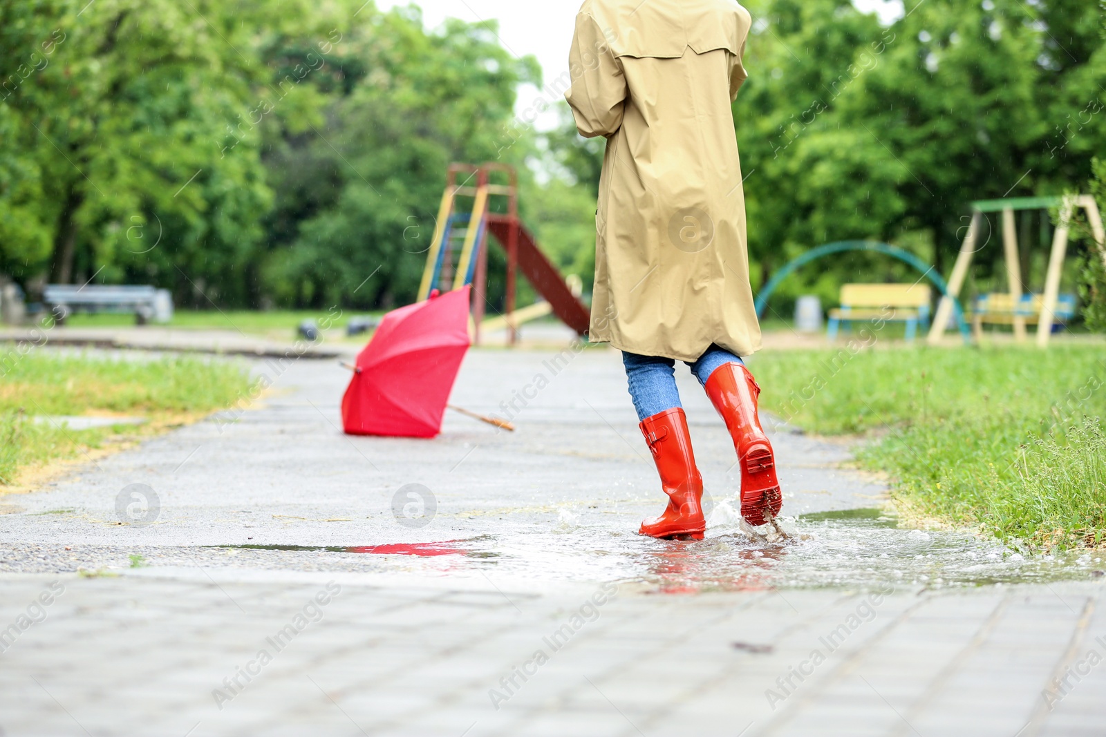 Photo of Woman in rubber boots running after umbrella on street, closeup. Rainy weather