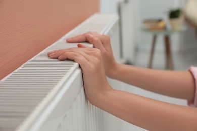 Photo of Woman warming hands on heating radiator indoors, closeup
