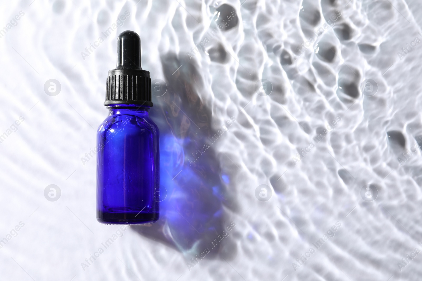 Photo of Bottle of face serum in water on white background, top view. Space for text