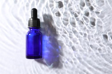 Bottle of face serum in water on white background, top view. Space for text