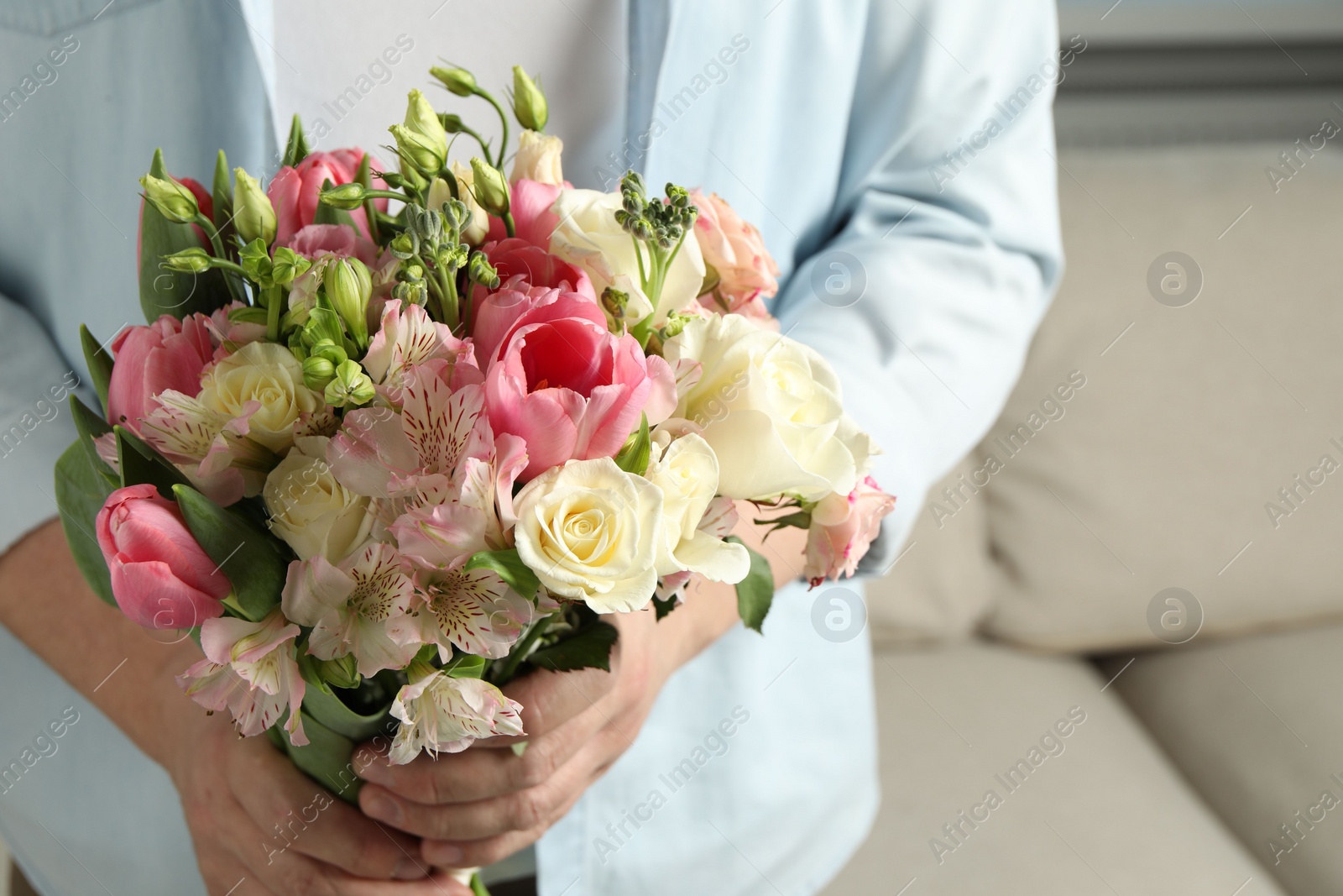 Photo of Man holding bouquet of beautiful flowers indoors, closeup