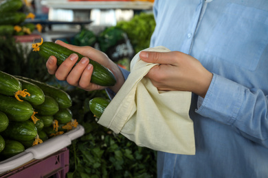 Woman putting cucumber into cotton eco bag at wholesale market, closeup. Life without plastic