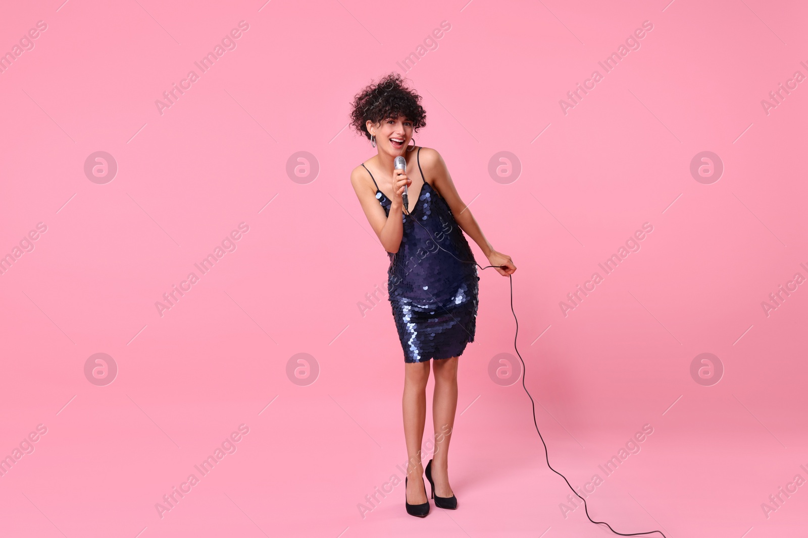 Photo of Beautiful young woman with microphone singing on pink background