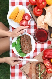 Photo of Woman eating steak at table outdoors, top view. Barbecue party