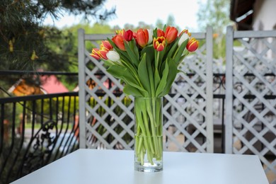 Photo of Beautiful colorful tulips in glass vase on white table at balcony