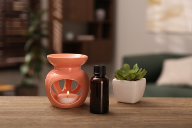 Photo of Aroma lamp with small candle, bottle of oil and houseplant on wooden table indoors