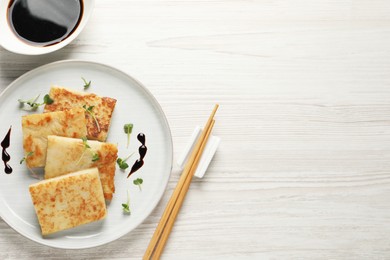 Photo of Delicious turnip cake and soy sauce served on white wooden table, flat lay. Space for text