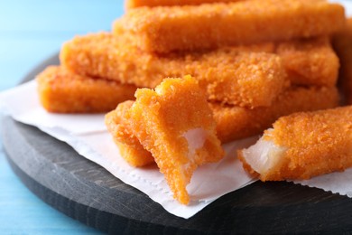 Photo of Fresh breaded fish fingers served on light blue wooden table, closeup