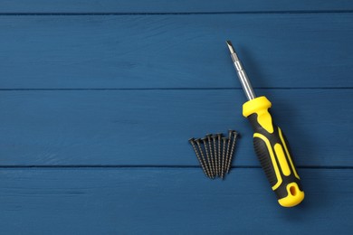 Photo of Screwdriver with black handle and screws on blue wooden table, flat lay. Space for text