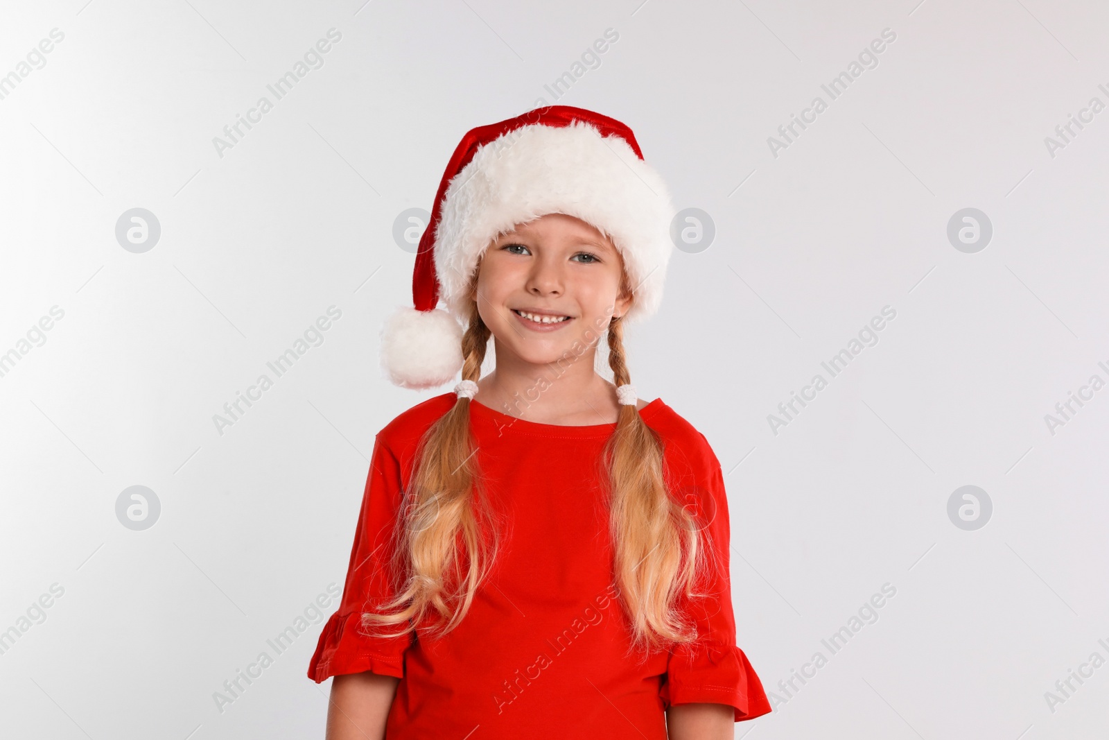 Photo of Happy little child in Santa hat on light grey background. Christmas celebration