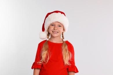 Photo of Happy little child in Santa hat on light grey background. Christmas celebration