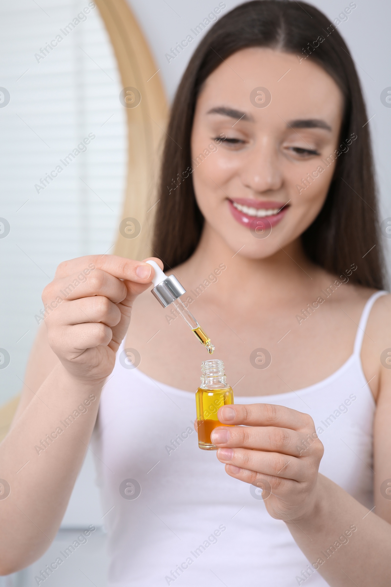 Photo of Young woman with essential oil in bathroom, selective focus